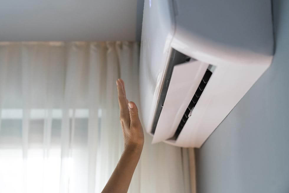 Foto einer Klimaanlage mit einer Hand davor, die den Luftstrohm fühlt